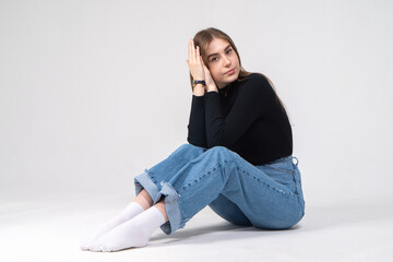 Young long haired girl posing while sitting. The model is wearing a black turtleneck and blue jeans