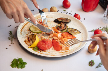 Hands with forks on a plate red fish with vegetables