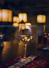 Reflection of the restaurant’s light rays and the surrounding space in a glass of white wine standing on a restaurant table