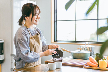 朝キッチンでコーヒーを淹れるエプロン姿のアジア人女性

