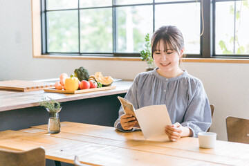 カフェで雑誌・フリーペーパーを読みながらコーヒーを飲むアジア人女性
