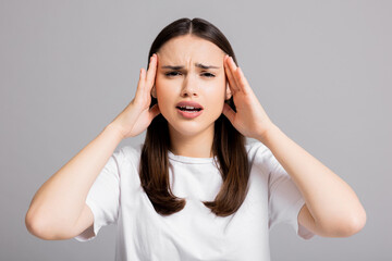Obraz premium Young beautiful brunette woman wearing white t-shirt over grey isolated background suffering from headache desperate and stressed because pain and migraine. Hands on head.