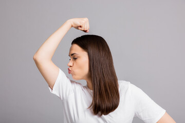 Successful young self made lady girl woman raising hand showing biceps kissing her biceps success gesture over white background wearing basic white t-shirt.