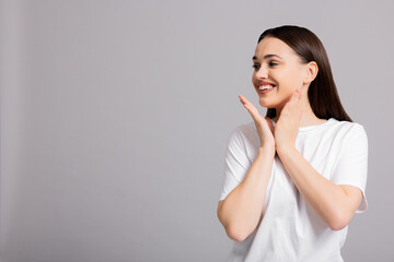 Happy young girl in casual basic white t-shirt standing near copyspace showing delighted curious happy funny emotions.