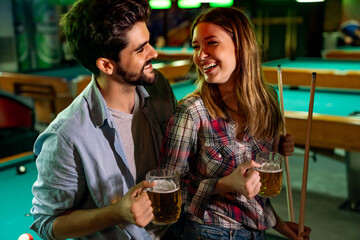Happy young couple enjoying while playing billiard in bar. People entertainment fun concept