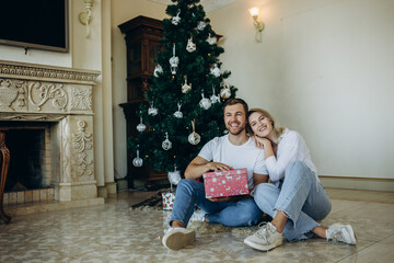 Obraz na płótnie Canvas family of four parents pregnant mom and dad and two siblings little boy and girl in stylish clothes in chalet are ready to welcome Christmas and New Year near Christmas tree with gift box presents