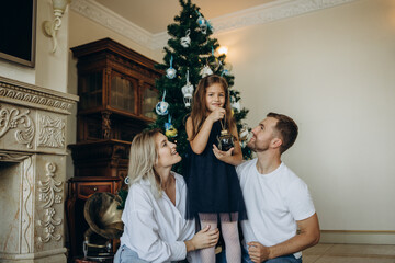 Merry Christmas and Happy Holidays. Cheerful mom and her cute daughters girls exchanging gifts. Parent and two little children having fun and playing together near Christmas tree indoors.