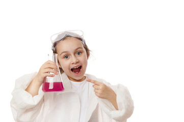 Inspired little girl points at flat-bottomed flask with chemical liquid, looks in amazement at camera, demonstrates the ongoing chemical reaction inside it, isolated on white background. Free ad space