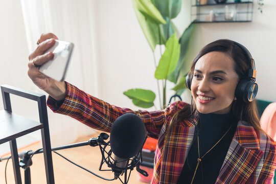 Young Latin American Female Singer Influencer Recording Song With Professional Setup Holding Up Phone And Smiling To Take Selfie. Horizontal Indoor Shot. High Quality Photo