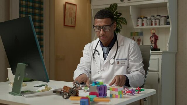 Pediatrician working online. African American kid's doctor working with toys on the desk.