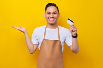 smiling young Asian man 20s barista employee wearing brown apron working in coffee shop, holding...