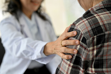 Professional Asian senior female doctor touches her young patient's shoulder, giving support