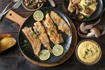 Pan fried fish with polenta and roasted mushrooms on wooden table. Flat lay