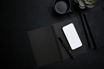 Modern trendy black workspace top view with smartphone mockup, pen, notebook, coffee cup