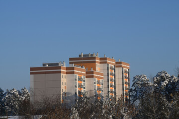 Modern architecture. New multi-storey and multi-apartment residential building. Neighborhood on the outskirts of the city. Winter, snow and pines