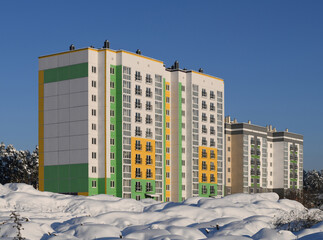 Modern architecture. New multi-storey and multi-apartment residential building. Neighborhood on the outskirts of the city. Winter, snow and pines