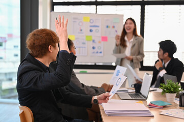 Back view of businessman raise hand ask question to presenter at meeting