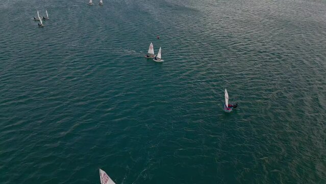 Training sailing yachts class optimist float on the sea.Yachting and sailing training. Summer sport. Aerial view top side of the blue sea and small training sailing yachts with athletes in the regatta
