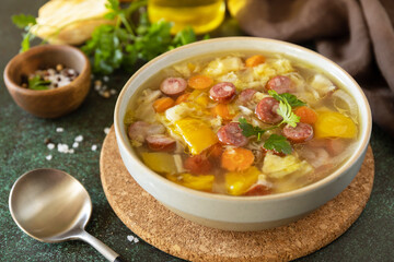 Traditional Zelnacka cabbage soup with sausages and vegetables in a bowl on a stone tabletop. Czech cuisine.