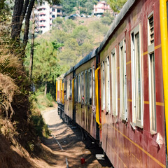 Obraz premium Toy Train moving on mountain slopes, beautiful view, one side mountain, one side valley moving on railway to the hill, among green natural forest. Toy train from Kalka to Shimla in India, Indian Train