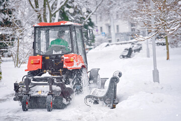 Snow removal red tractor clean walkway in park with plough and sweeping brush. Tractor removing snow, cleaning sidewalk from snow during blizzard. Tractor clear snow, machinery cleaning equipment - obrazy, fototapety, plakaty