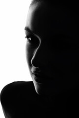 Fashion and make-up concept. Close-up dark face silhouette of beautiful and sexy woman. Part of model face illuminated with light. Sensual mood. Cheek is in camera focus. Black and white image
