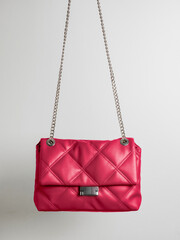 Quilted crossbody bag in red Viva Magenta color with metal chain strap on neutral light background....