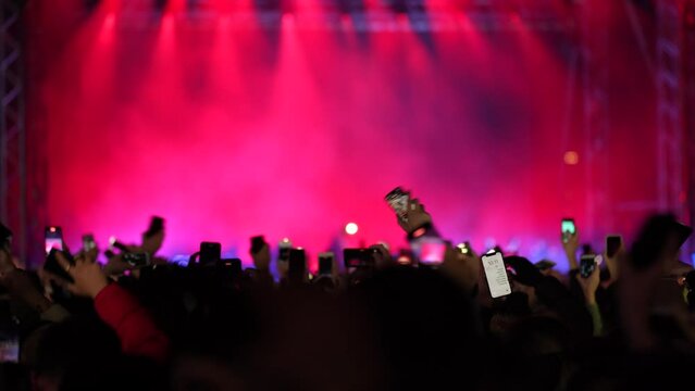 Crowd of fans waving smartphone flashlights on a live music concert with illuminated stage