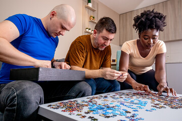 Friends playing with jigsaw puzzle at home, on a white wooden table. Putting things together and solving problems. Fun and diversity in friendship.