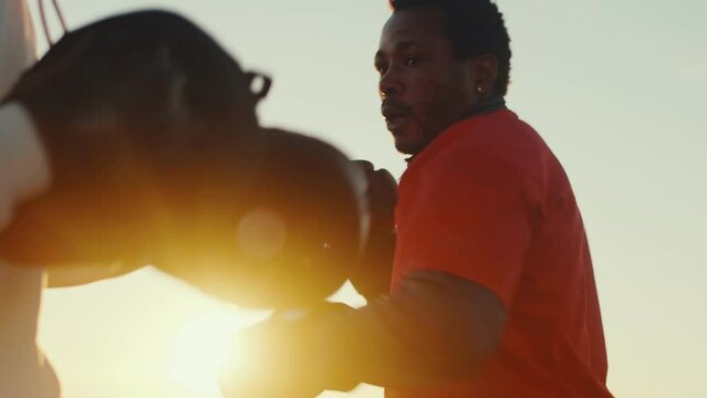 Two black athletes in boxing gloves practice punches and dodges in sparring outdoor on the sunset close up. Two boxers doing few training exercises