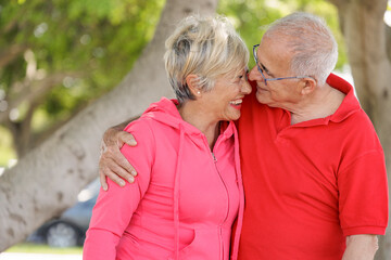 coppia di anziani con abiti sportivi molto sgargianti  si abbraccia felice in un parco