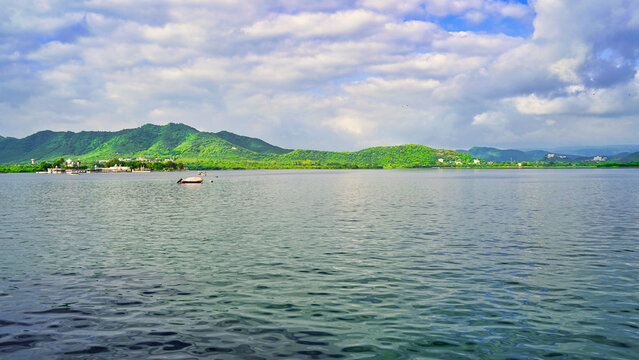 Lake Pichola with cloudy sky and aravali hills background in Udaipur, Rajasthan, India. An artificial lake popular for boat riding among tourist, created in year 1362. City of lakes. White Lake palace