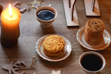 Two types of cookies, cups of tea or coffee, various Christmas decorations and lit candles. Cozy Christmas atmosphere at home. Selective focus.