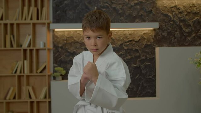 Portrait of motivated adorable multiracial elementary age athlete kid in karate kimono making karate rie and gesture, standing in front stance, ready to fight , expressing determination and confidence