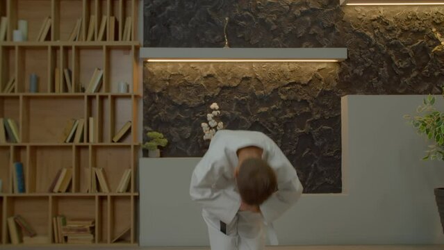 Determined motivated multiethnic school age karate boy in karate gi making ritual bow and gesture before practicing sport training , expressing respect to rival and sportsmanship in domestic room
