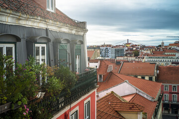Obraz premium historic buildings of the old town of lisbon. Old colorful buildings, narrow streets, historic churches. Tiled roofs. View from the top of the viewpoint on the tenement houses and monuments. Clouds