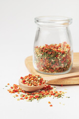 Mixed pieces of dried vegetables in wooden spoon  and glass jar on wooden stand isolated