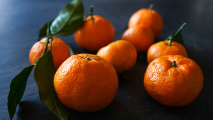 closeup of fresh mandarin oranges fruit or tangerines with leaves on dark stone table 