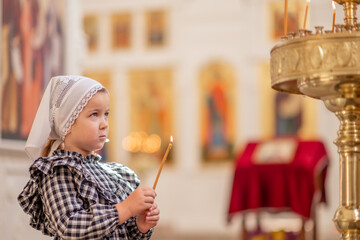 a little Christian girl in an Orthodox church puts a candle, prays in front of the icon. High...