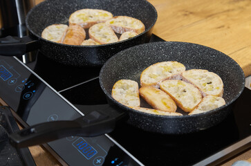 Two frying pans with toasted bread slices on the stove