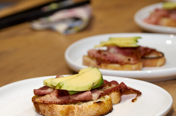 Toast with bacon and avocado on a plate standing on a wooden table