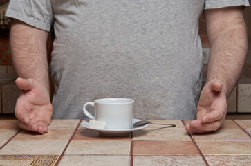 Human hands point to a coffee cup with a small spoon and sugar cubes on a saucer, standing on a...