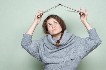 A woman hides under a book, as if under a roof from hostile factors: stress, depression, fear