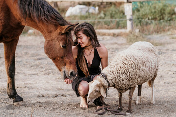 Girl with dreadlocks sitting with a horse and with a sheep.