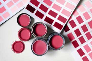 Tiny sample paint cans during house renovation, process of choosing paint for the walls, different red colors, color charts on background. Viva Magenta, color of the year 2023 - obrazy, fototapety, plakaty