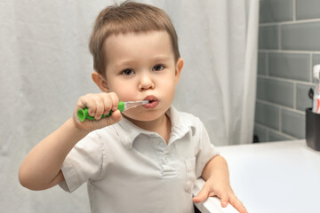 a boy of 3 years old holds a toothbrush and brushes his teeth in the bathroom, daily routine, dental care