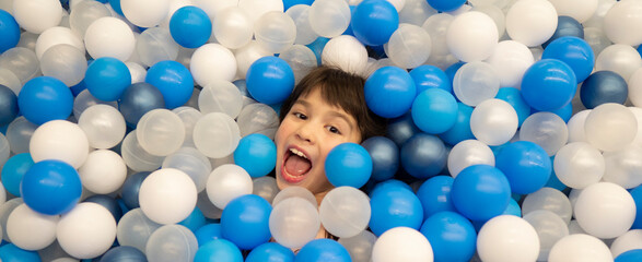 Banner happy little girl having fun in playroom. Kid lying on blue and white plastic balls in big...