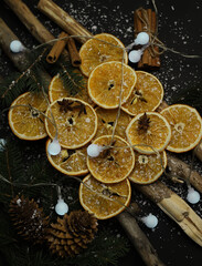 Obraz na płótnie Canvas dried oranges cones cinnamon fir branches and star anise beautifully laid out on wooden natural sticks christmas decoration on a dark background with snow and garlands. for cards calendar labels signa