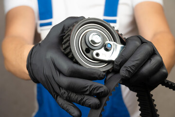 Car mechanic in blue jumpsuit holds oil filter of car in his hands and rotates it in black gloves....