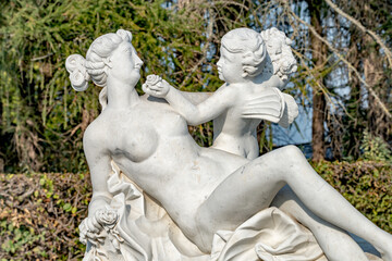 Old statue of a sensual Renaissance era beautiful woman after bathing with an angel in a city park of Potsdam, Germany, details, close up